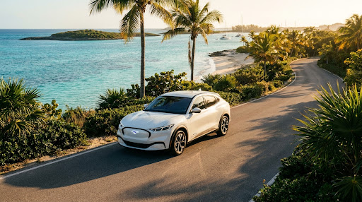 White Mustang Mach-E driving on a coastal road in the Bahamas at sunset.